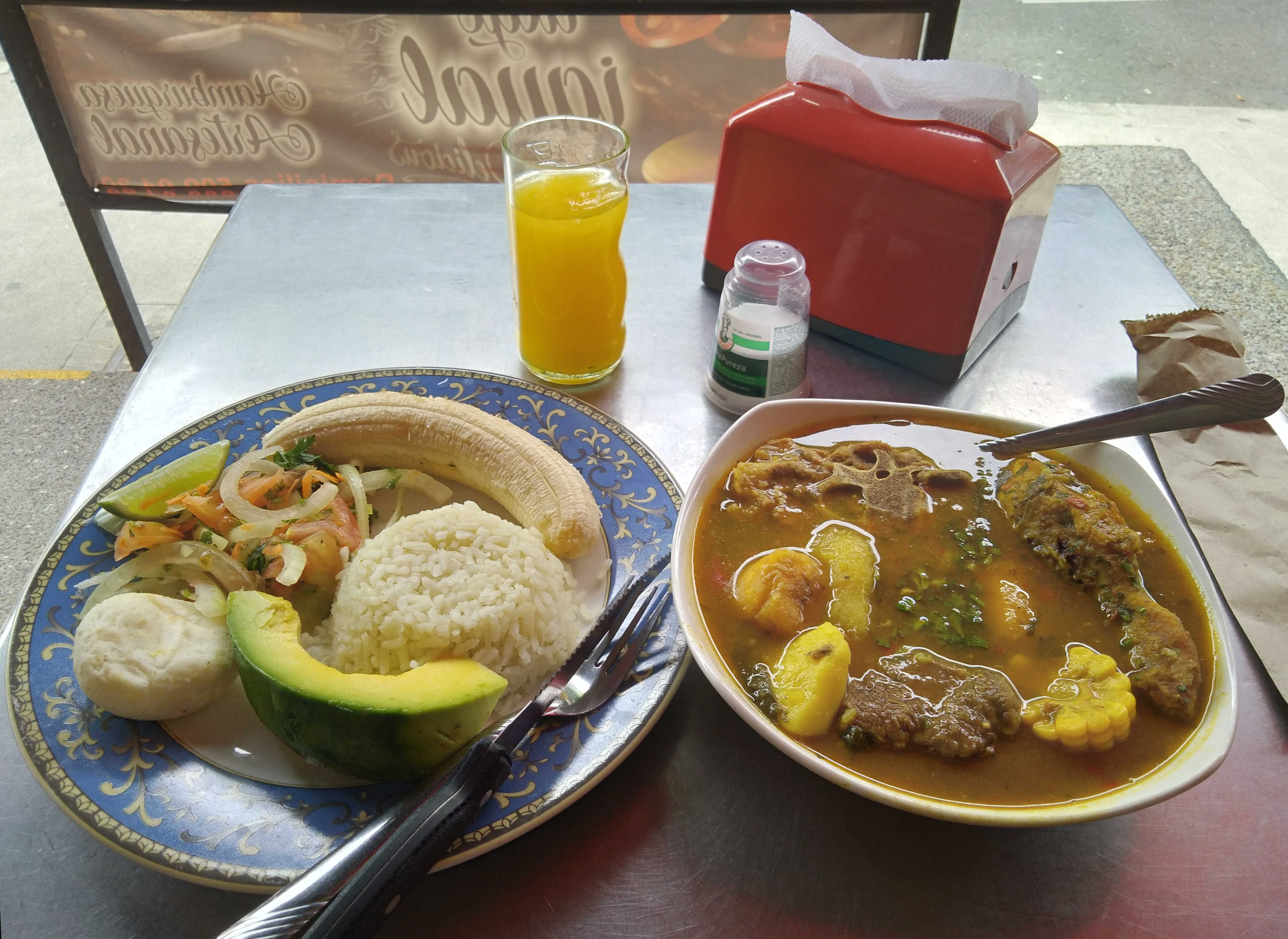 ''Sancocho'' dominical à Medellín : bœuf, poulet, os de porc, manioc, plantain, pomme de terre, ''mazorka'' (épi de maïs), légumes ; et son accompagnement : riz blanc, avocat, ''arepa'', salade composée, banane crue – prix : environ 3,3 euros